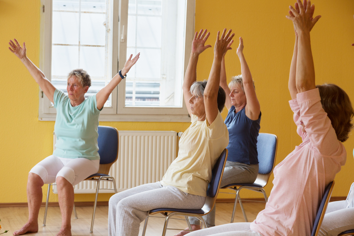 active senior women in yoga class exercisig on chairs