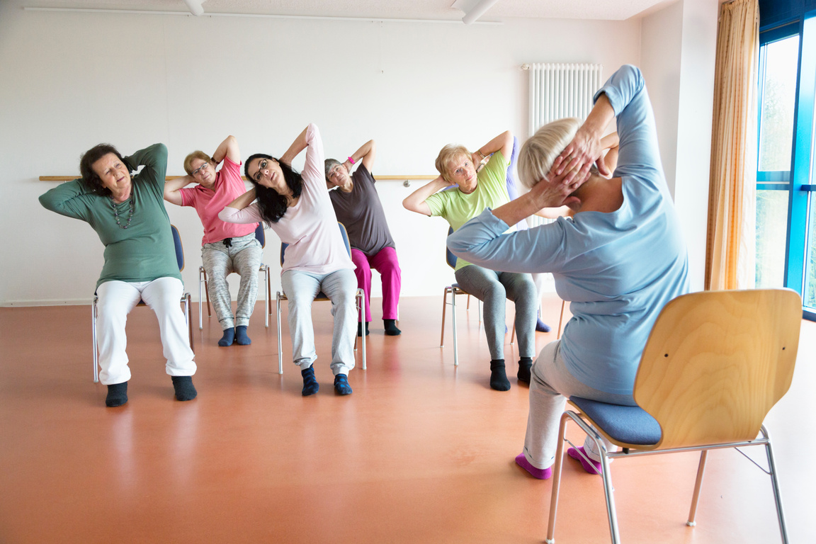 teacher and active senior women yoga class on chairs